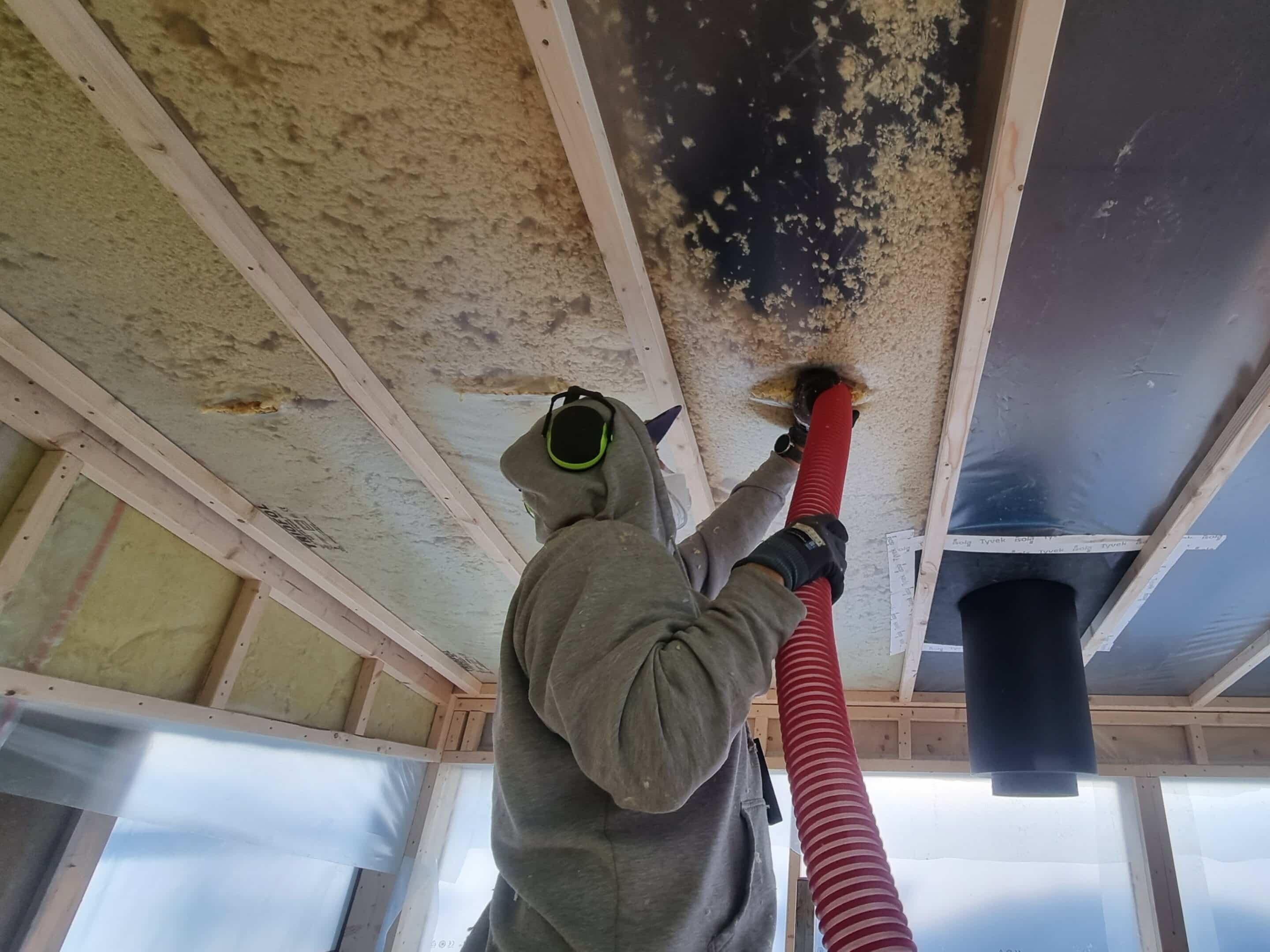 A carpenter in a protective suit blowing insulation in under a floor