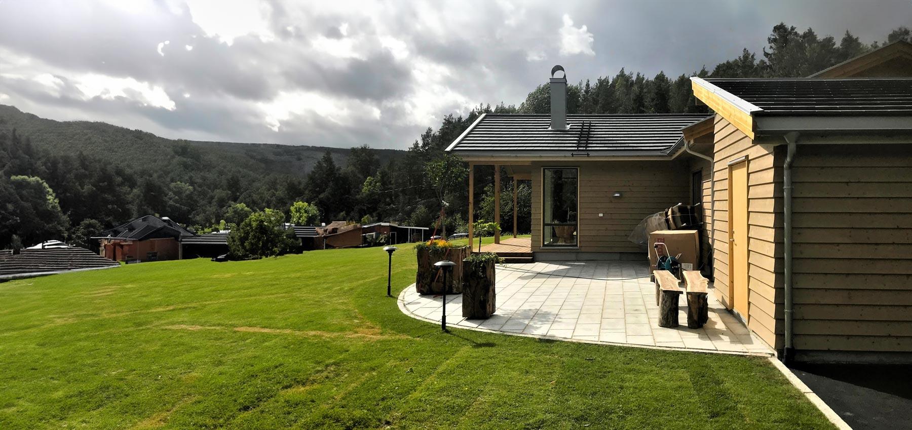 A new house with a stone terrace and lawn, wooded hills behind